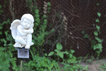 ceramic small white figure of an angel with a flashlight in the green grass. flashlight in the...