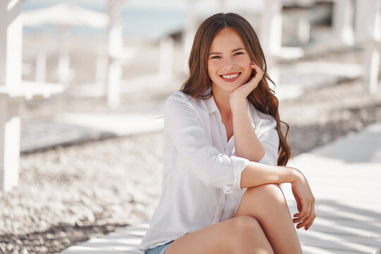 Pretty woman on the beach at summer white shirt and denim shorts wooden background sitting on floor long hair
