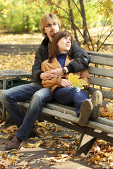 Fototapeta premium A young couple in love is sitting on a Park bench. Bright and warm autumn day.