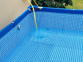 Swimming pool in the garden. Backyard pool is filled with clean water from a hose.
