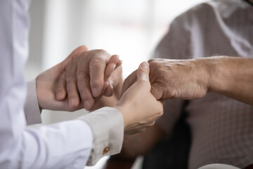 Close up caring doctor therapist gp holding older man patient hands at meeting, female caregiver supporting comforting mature man, professional psychological help, empathy, warm relationship