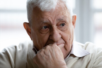 Head shot thoughtful upset elderly man thinking about problems, touching chin, mature widower lost...
