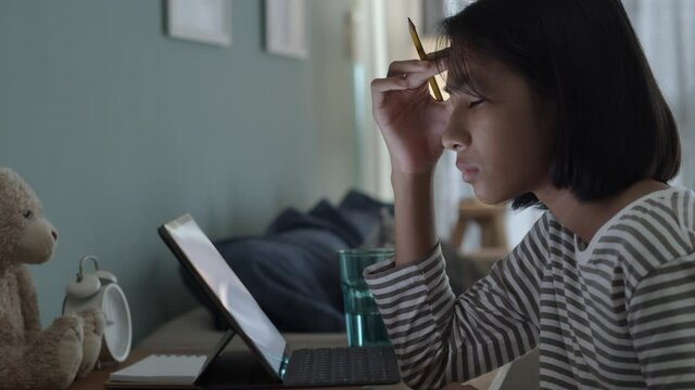 Boring Asian girl is studying online via the internet on tablet at home 