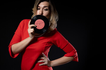 Obraz premium girl in a red dress with vinyl records in hands on a black background, copy space