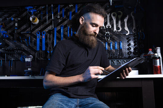 Stylish bicycle mechanic making notes in clipboard in workshop. theme small business selling, repair and service bicycles. Technician Doing Administrative paperwork in bike shop. Manage business