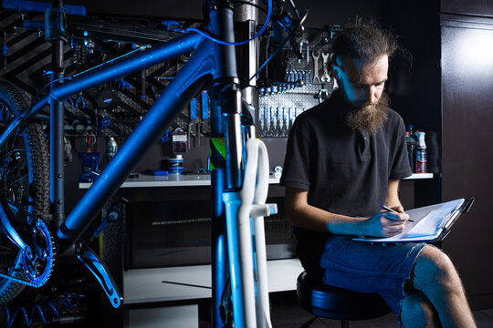 Bicycle Workshop Technician Doing Administrative Work. Bicycle mechanic writing in his checklist notebook. Bicycle mechanic at work. Caucasian worker writing on clipboard in bicycle shop