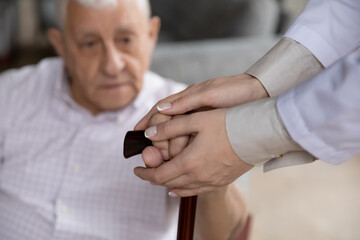 Close up female caregiver holding mature patient hands on cane, caring doctor therapist supporting comforting elderly disabled man, expressing care and empathy, healthcare and psychological help