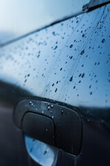 Drops of rain flow down the door of a blue car close-up.