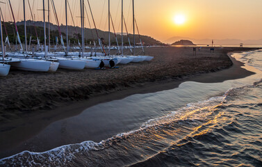 Sunrise at the beach. Sailing catamarans stand on the sand, the sun rises over the mountains. Back light.