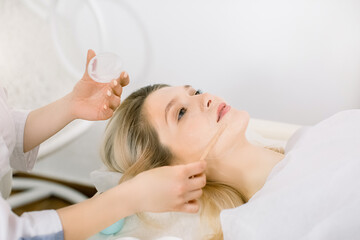 Obraz na płótnie Canvas People, beauty, spa, cosmetology and skincare concept. Close up of beautiful young woman lying on the couch and female doctor cosmetologist applying facial mask by wooden spatula in spa center