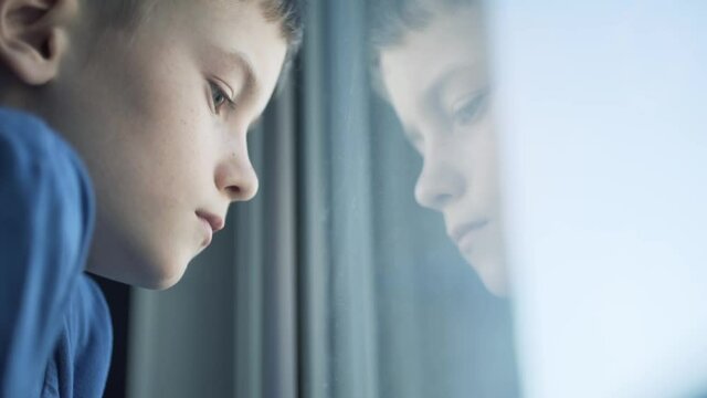 Sad unhappy kid standing near the window. Upset boy.