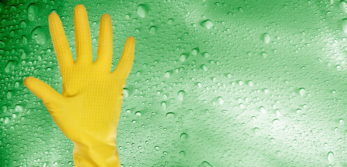 close up hand wearing yellow cleaning gloves over water drops covered background