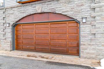 Arched brown wood panel garage door of home with stone brick exterior wall