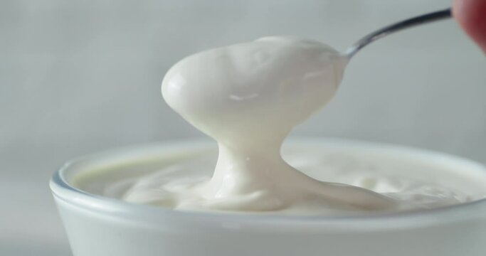 Man's hand with a spoon takes the sour cream from bowl.
