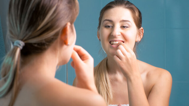 Young woman cleaning and checking her teeth at mirror in bathroom