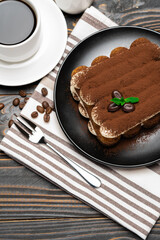Classic tiramisu dessert on ceramic plate, milk or cream and cup of coffee on wooden background