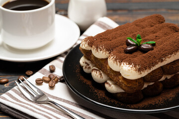 Classic tiramisu dessert on ceramic plate, milk or cream and cup of coffee on wooden background