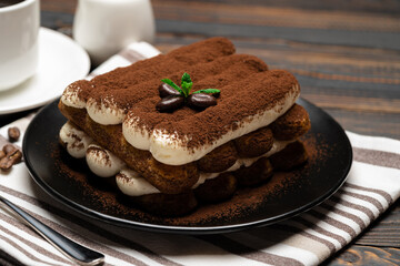 Classic tiramisu dessert on ceramic plate, milk or cream and cup of coffee on wooden background