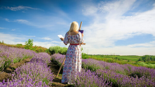 Beautiful young woman drawing picture on lavender field at morning