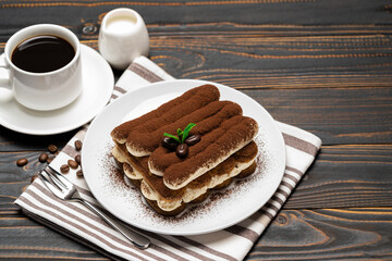 Classic tiramisu dessert on ceramic plate, milk or cream and cup of coffee on wooden background