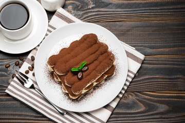 Classic tiramisu dessert on ceramic plate, milk or cream and cup of coffee on wooden background