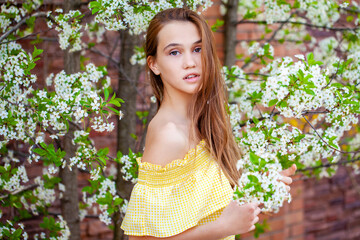 Young red-haired woman posing against the backdrop of a blossoming apple tree