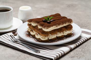 Classic tiramisu dessert on ceramic plate, milk or cream and cup of coffee on concrete background