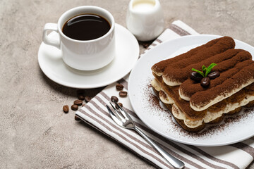 Classic tiramisu dessert on ceramic plate, milk or cream and cup of coffee on concrete background