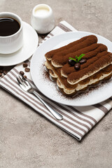 Classic tiramisu dessert on ceramic plate, milk or cream and cup of coffee on concrete background
