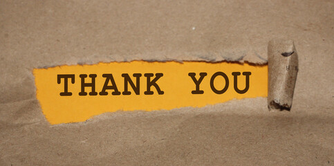 The text Thank You appearing behind torn brown paper