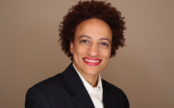 Attractive Successful Mature Black Business Woman With Natural Hair Smiling And Wearing A Dark Suit And White Shirt. Neutral Background.