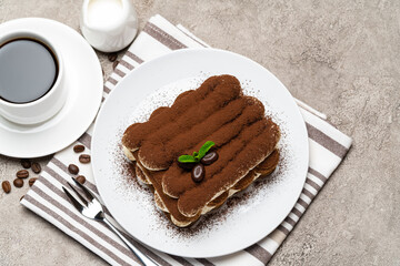 Classic tiramisu dessert on ceramic plate, milk or cream and cup of coffee on concrete background