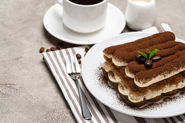 Classic tiramisu dessert on ceramic plate, milk or cream and cup of coffee on concrete background