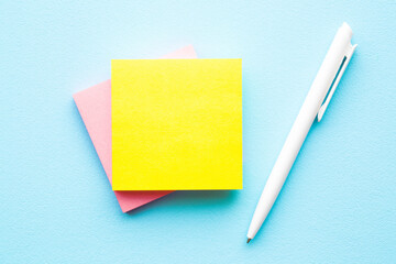 Bright yellow and pink sticky notes and white pen on light blue table background. Pastel color. ...