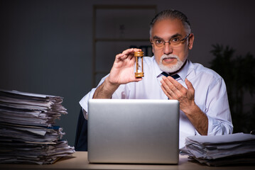 Old male employee working late at workplace