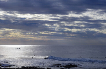 Surfers sit under a cloudy sky with waves
