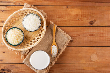 Rice milk and rice seeds on wooden boards. Rice milk in glass on sackcloth. Vegan non-dairy milk on wooden background. Alternative milk from rise. Rustic style. Top view