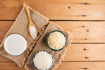 Rice milk and rice seeds on wooden boards. Rice milk in glass on sackcloth. Vegan non-dairy milk on wooden background. Alternative milk from rise. Rustic style. Top view