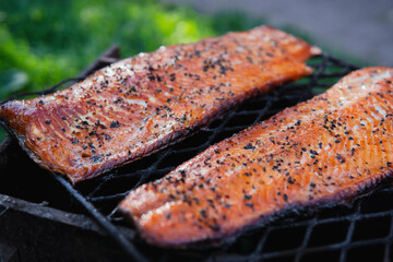 Hot smoked salmon fillets with sesame seeds, paper and spices on black grille. Freshly smoked barbecue tasty fish. Healthy seafood concept. Selective focus, open air. Copy space, recipe, close up view