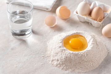 pile of whole grain flour with an egg, a glass of water, eggs and eggshells on the kitchen table. Cooking process. horizontal image. selective focus. place for text