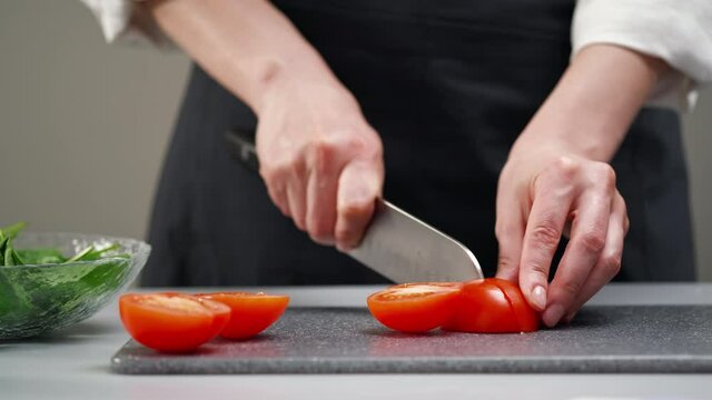 A female chef in a white uniform and a black apron in the restaurant kitchen. Preparing food. The cook cuts the vegetables with a large kitchen knife.
