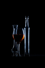 Copa de vino llena y dos botellas de vidrio vacías sobre fondo negro, iluminadas con flash