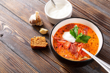 borscht with parsley and sour cream on a brown wooden background,  spoon, bread, sauce bowl, garlic