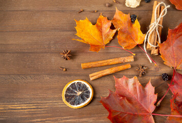 yellow and  red  autumn maple leaves, cinnamon sticks, anise, a slice of dried orange on a brown wooden background top view close up
