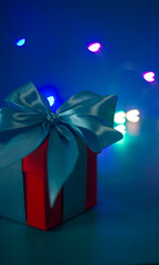 red gift box with a blue ribbon on a blue background with colored lights