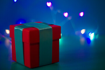 red gift box with a blue ribbon on a blue background with colored lights