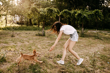 Young woman running with her dog, playing on green grass in a park.