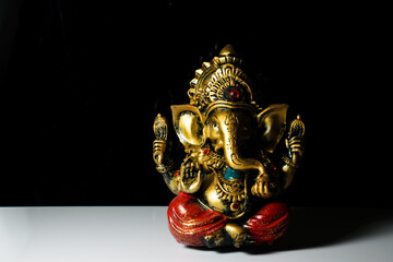 An isolated sculpture of the Indian god Ganesha placed on a reflective white table in a dark background