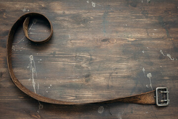 Old leather belt on aged wooden table background with copy space.