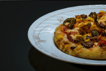 Vegetable pizza placed on a white plate and kept on a black table with space for text in the left